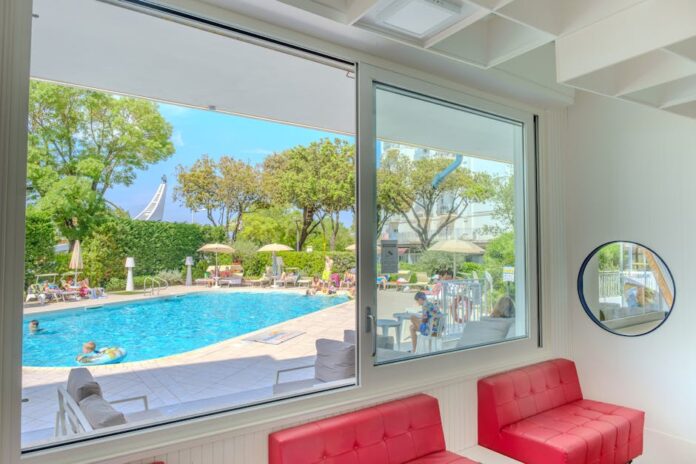 familotel sonnenpark - View of a vibrant summer pool scene from a stylish indoor hotel lounge.